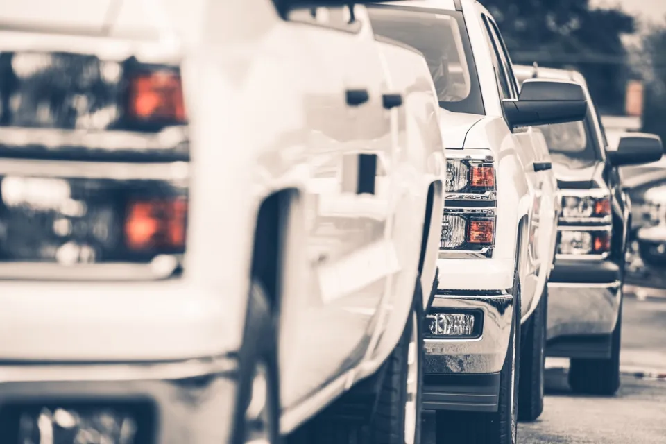 Close-up of white pick-up truck on sales lot from front driver's side; two more trucks behind it